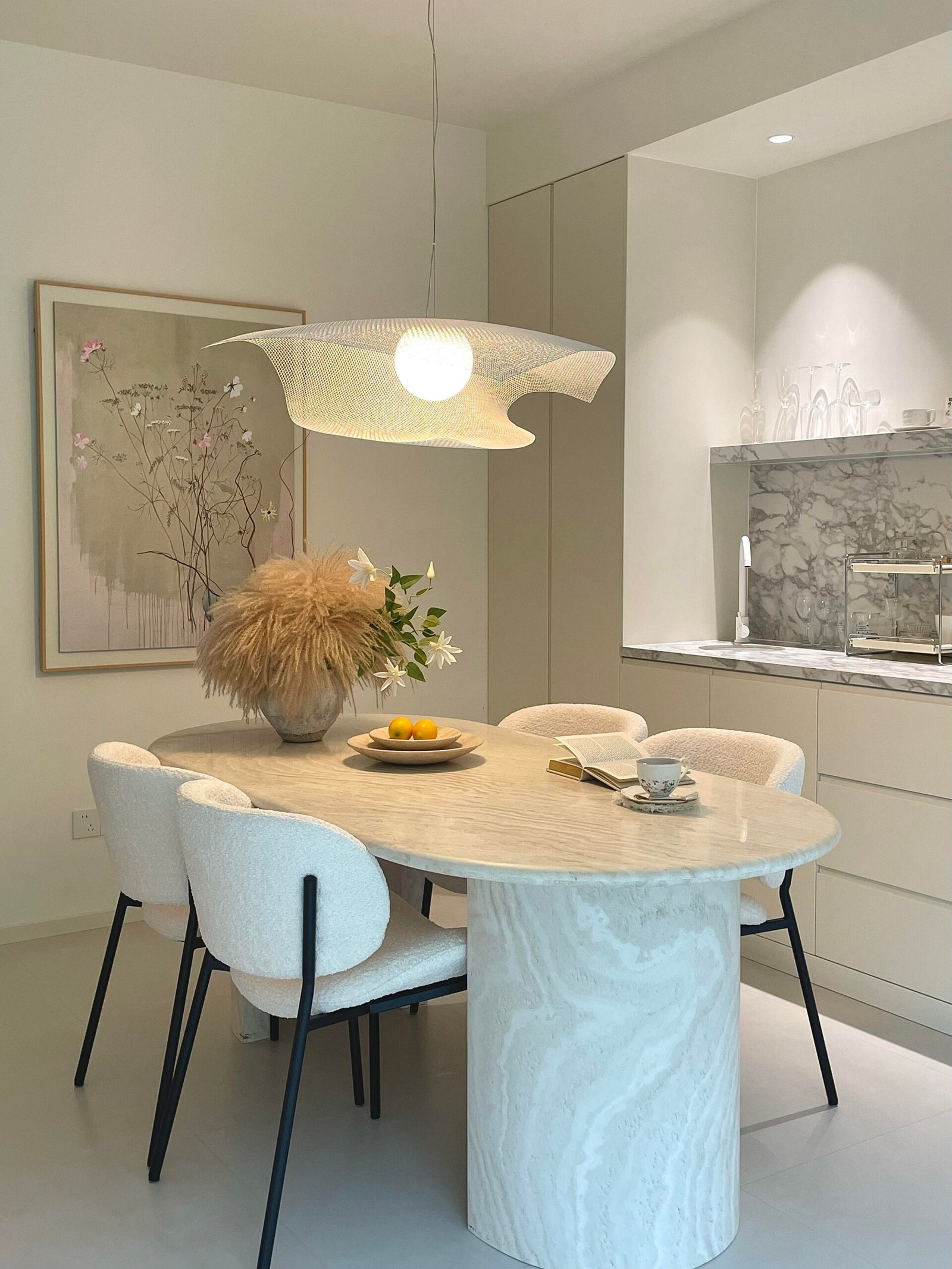 Oval marble Dining Table Set for 4 with cream boucle chairs and sculptural pendant light.