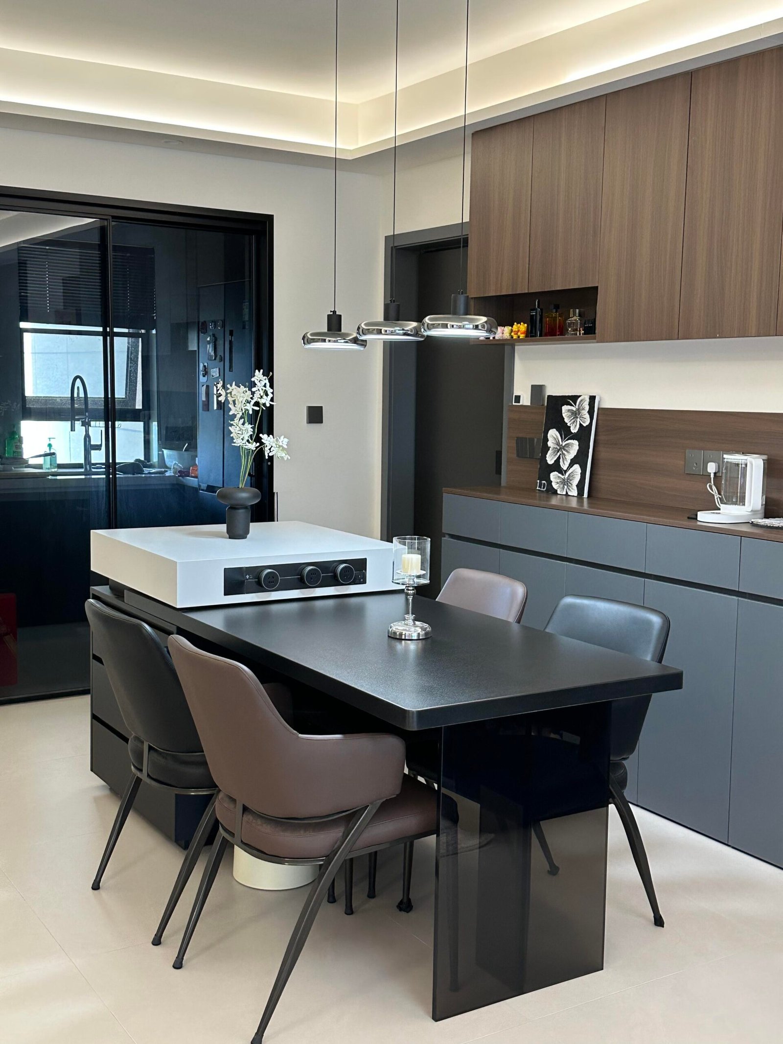 Dark wood kitchen with black dining furniture and warm ambient ceiling lighting.
