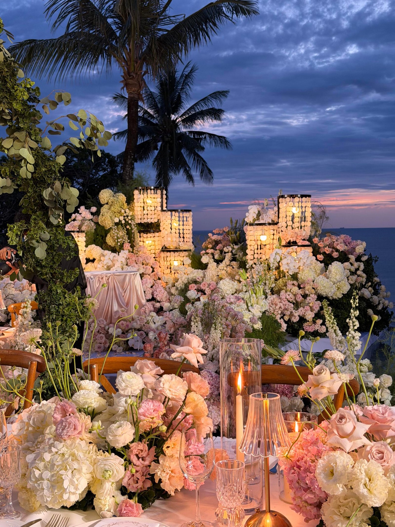 Crystal chandelier hanging above wedding table under palm tree canopy